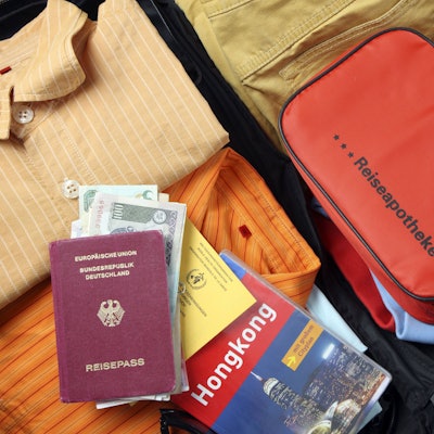 Auf einem gepackten, geöffneten Koffer liegt ein Medizin-Täschchen mit der Aufschrift Reiseapotheke