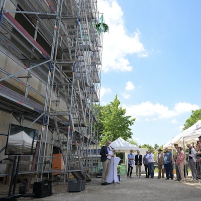 Vor dem eingerüsteten Rohbau stehen Kinder, der Bürgermeister hält eine Rede.