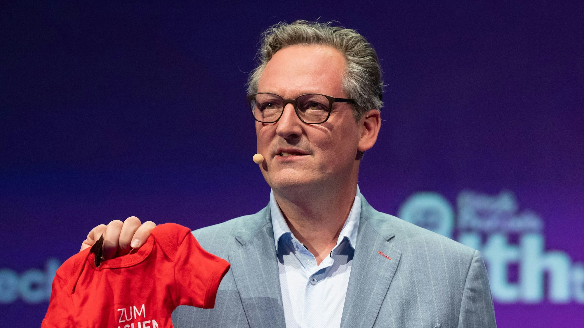 Eckart von Hirschhausen hält einen Babybody hoch.