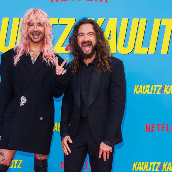 Bill und Tom Kaulitz stehen vor einer Wand mit dem Slogan ihrer Netflix-Doku und grüßen in die Kamera