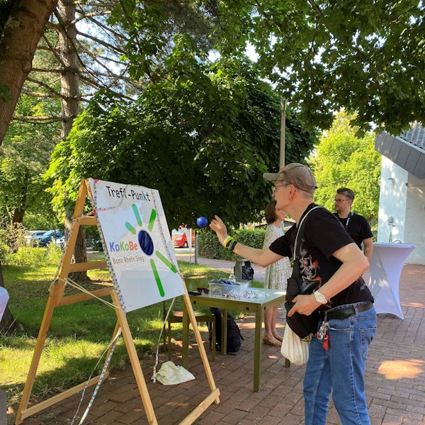Ein Mann wirft Bälle auf eine bunt gestaltete Tafel mit der Aufschrift "Treff-Punkt"
