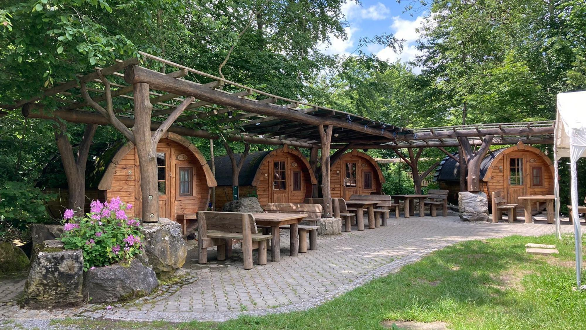 Eine Ansammlung von Holzfässern, die als Unterkunnft dienen, stehen in einem Garten.