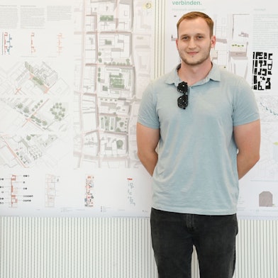 Die Kölner Studierenden Jana Passetschnik und Frederick Cornelius stehen vor einem Plakat ihres Entwurfs für die Umgestaltung der Kölner Innenstadt.