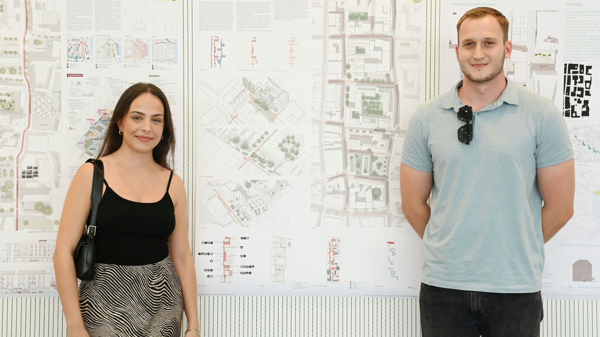 Die Kölner Studierenden Jana Passetschnik und Frederick Cornelius stehen vor einem Plakat ihres Entwurfs für die Umgestaltung der Kölner Innenstadt.