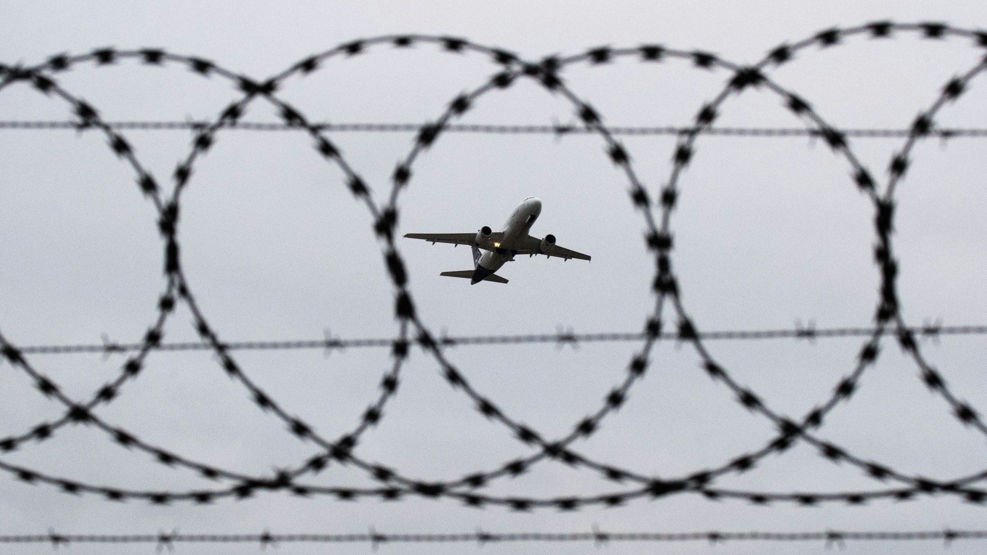 Ein Flugzeug startet am Flughafen Hannover, fotografiert durch Stacheldraht am Flughafenzaun. (Symbolbild)