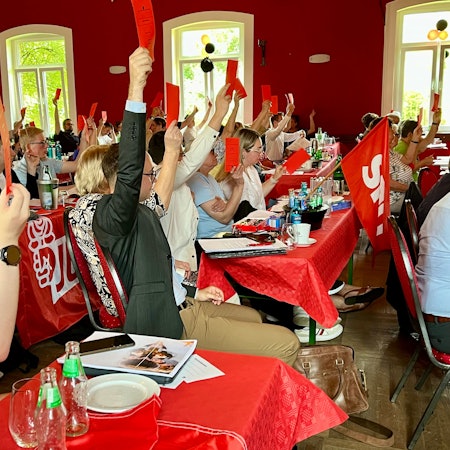 SPD-Mitglieder halten im Rheindorfer Saal Norhausen rote Stimmkarten hoch.
