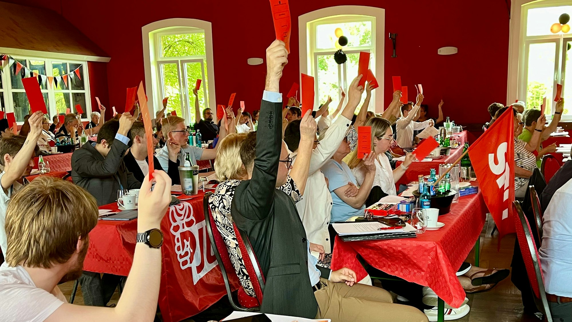SPD-Mitglieder halten im Rheindorfer Saal Norhausen rote Stimmkarten hoch.