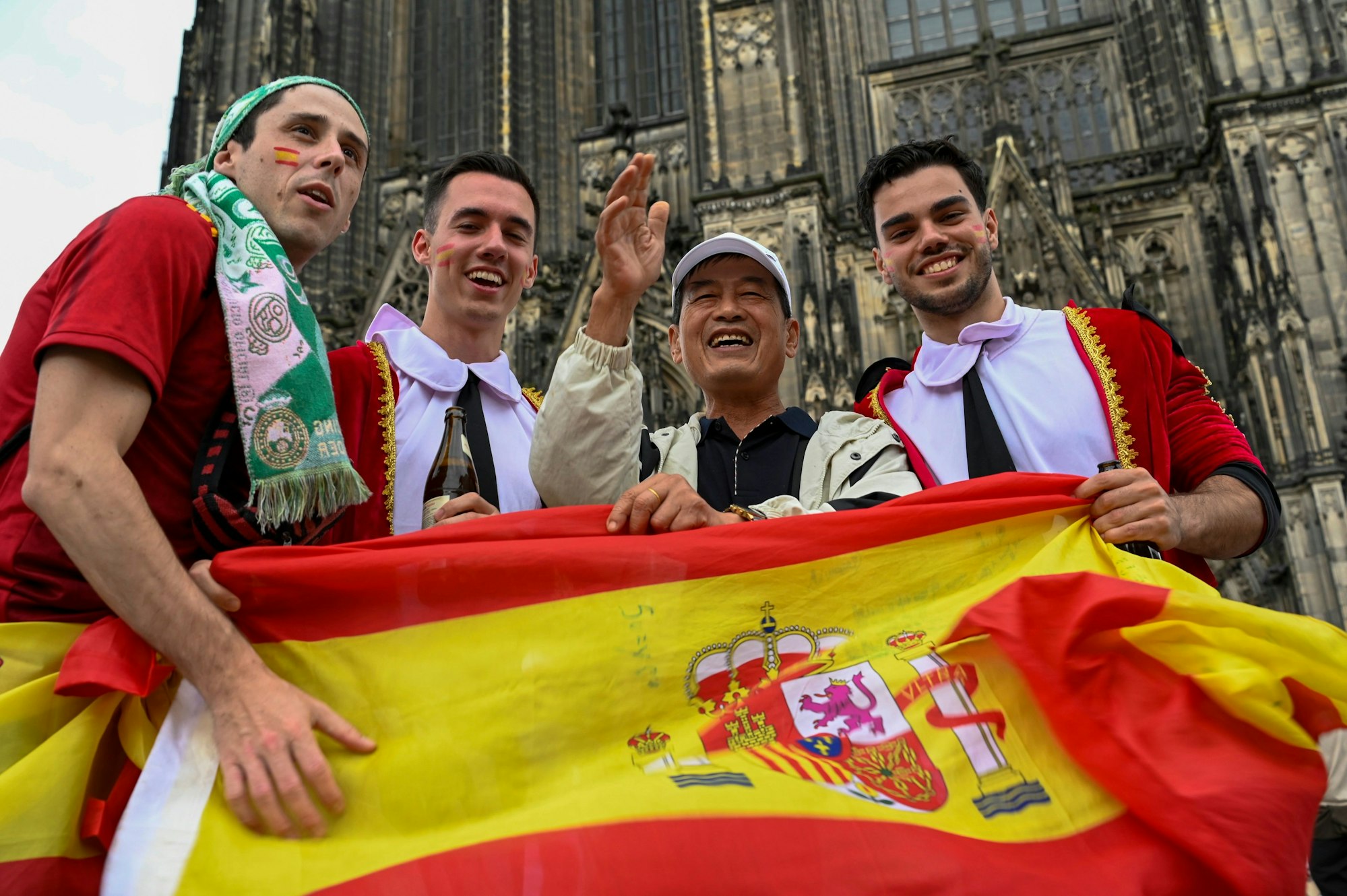 Vier Männer stehen lachend nebeneinander, vor sich halten sie eine spanische Flagge.