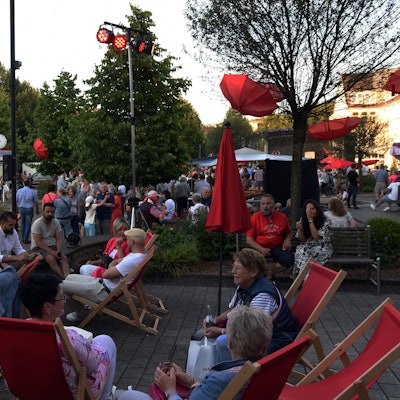 Menschen sitzen beieinander auf roten Liegestühlen.