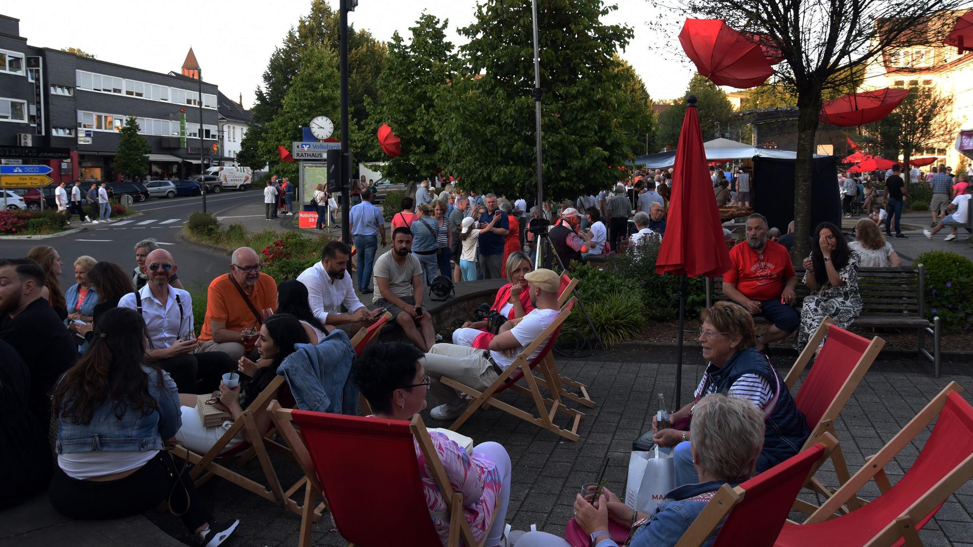 Menschen sitzen beieinander auf roten Liegestühlen.