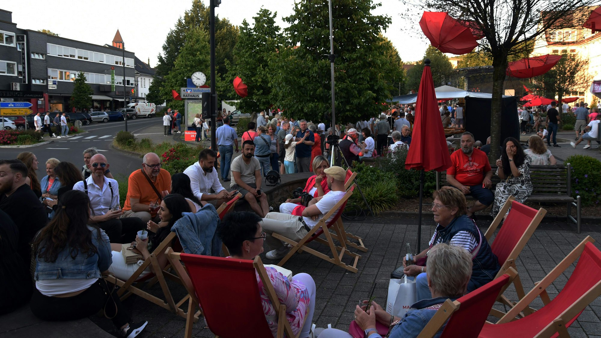 Menschen sitzen beieinander auf roten Liegestühlen.