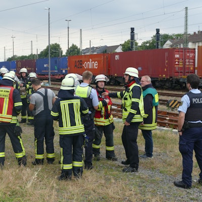 Feuerwehrleute stehen neben Bahngleisen.