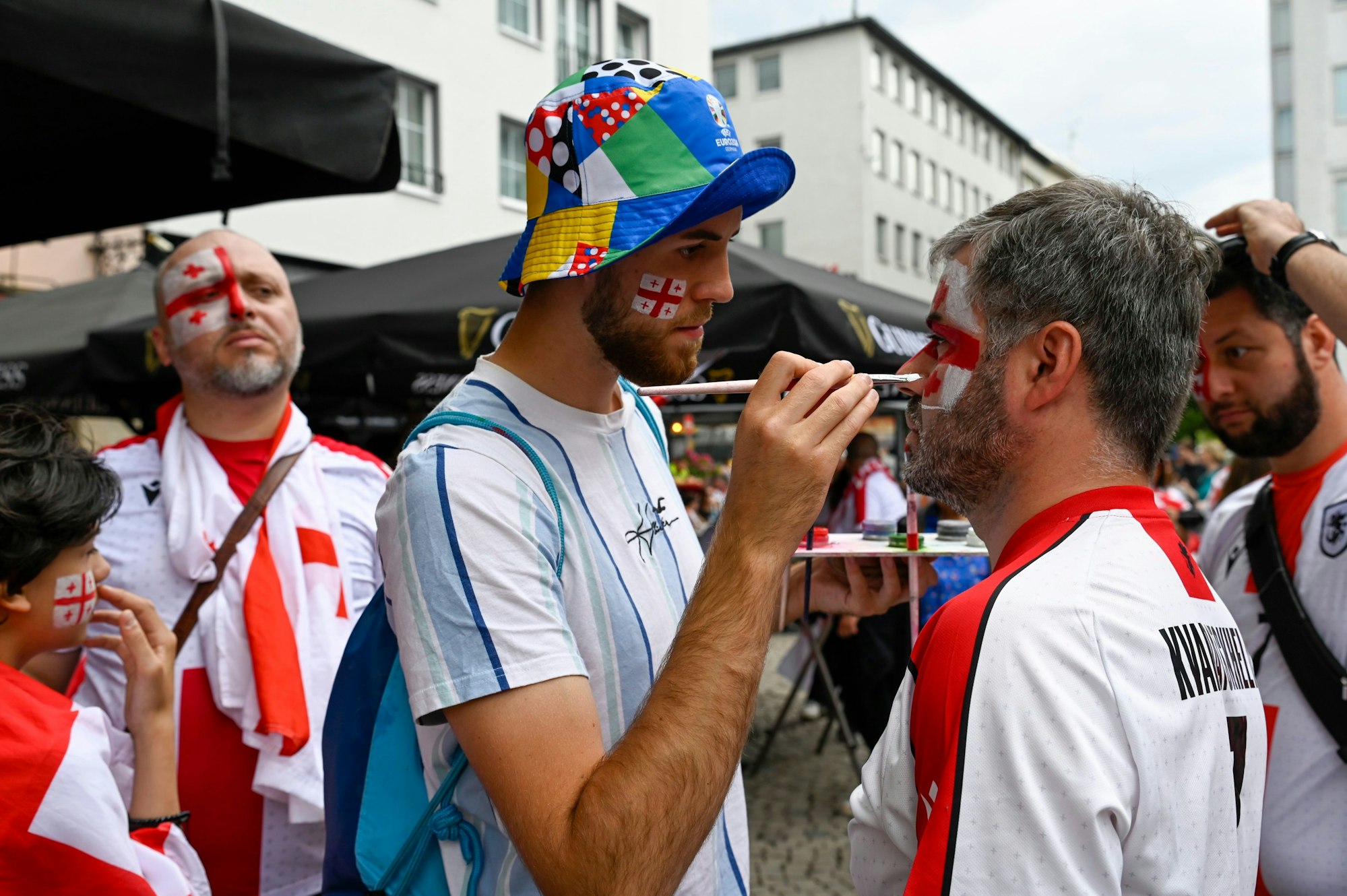 Ein Mann malt einem anderen Mann eine georgische Flagge ins Gesicht.