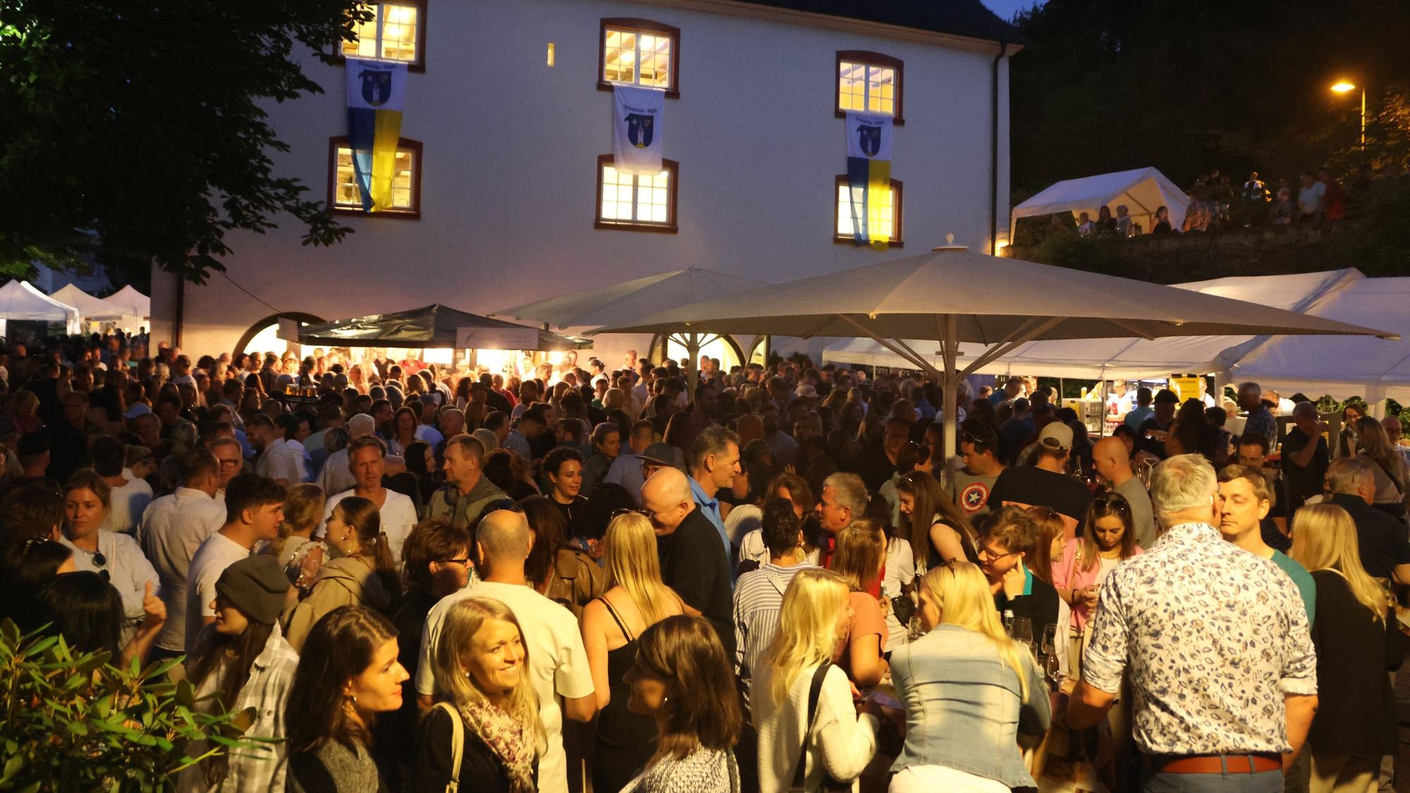 Eine große Menschenmenge in der Dämmerung vor dem Burghaus.