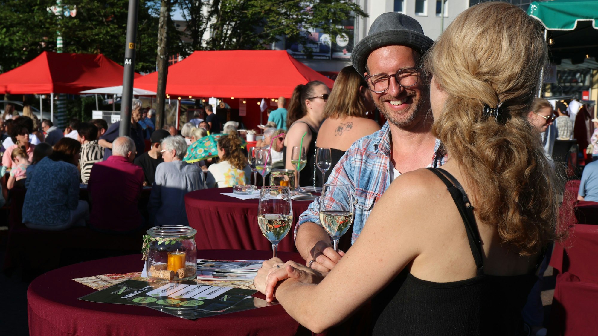 Ein Mann und eine Frau mit Weingläsern an einem Stehtisch.