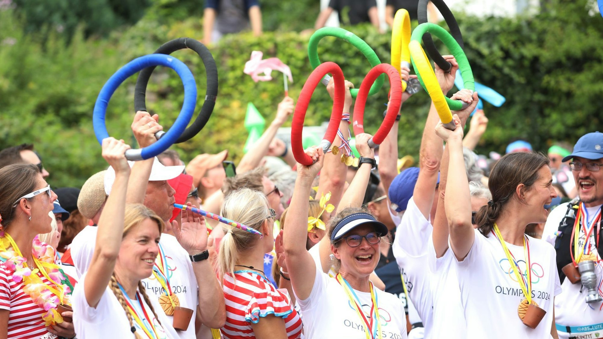 Lachende Menschen in Olympia-Trikots halten bunte Ringe in die Höhe.
