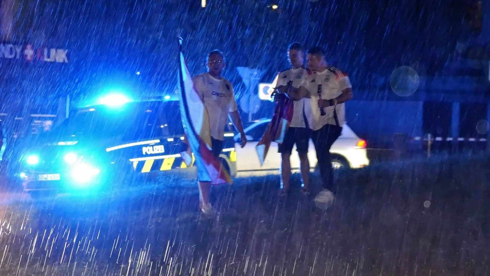 Drei Fußballfans stehen im strömenden Regen in der Mitte des Europakreisels in Euskirchen.