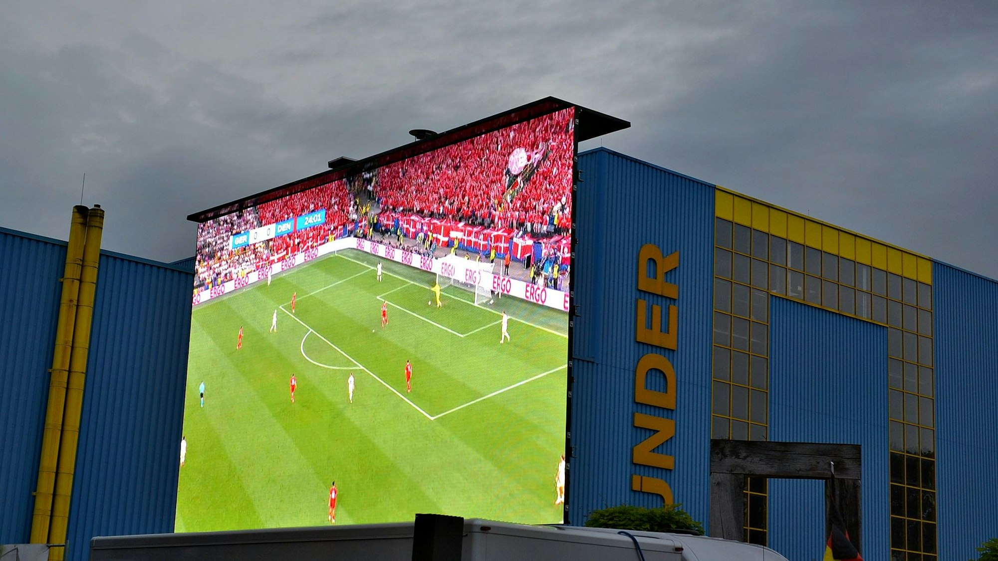 Hinter dem am Bünder-Firmengebäude befestigten Großbildschirm ziehen dunkle Wolken am Himmel über Euskirchen auf.