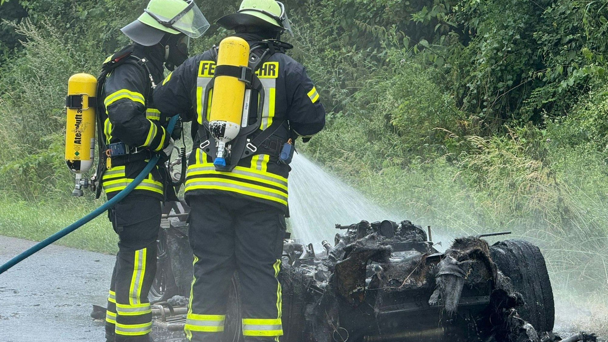 Zwei Feuerwehrleute mit Atemschutzgerät löschen ein ausgebranntes Trike auf der Autobahn A3 vor Bad Honnef.