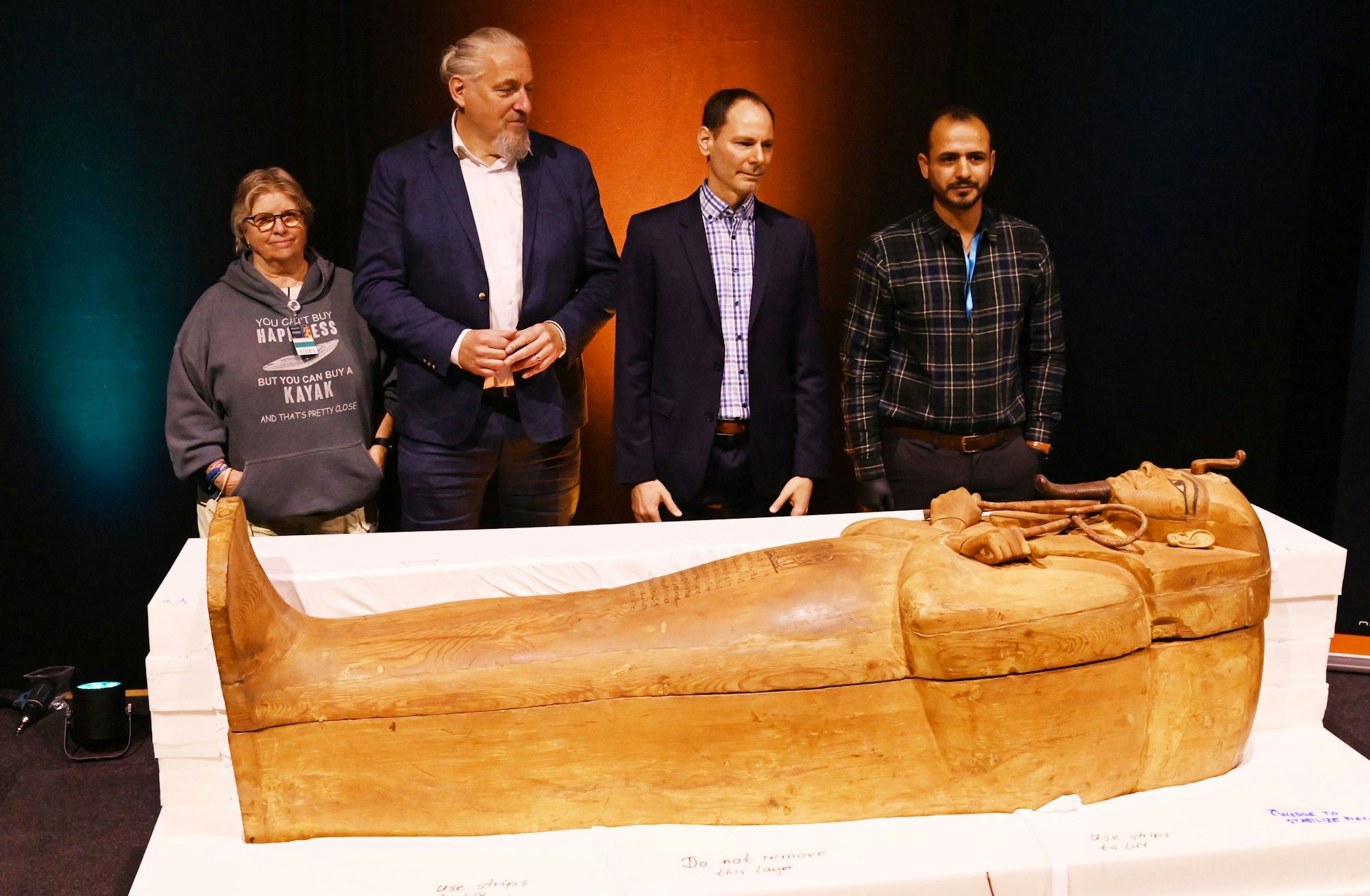 Vier Männer stehen hinter einem Holzsarg.