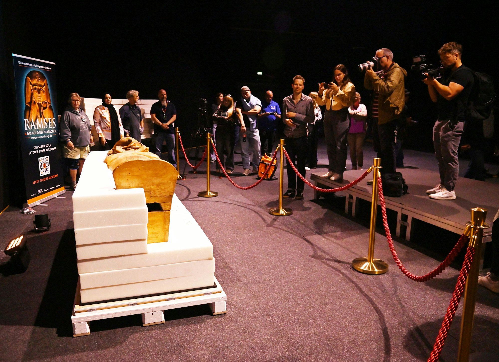 Menschen stehen auf einem Podest und fotografieren einen Holzsarg.