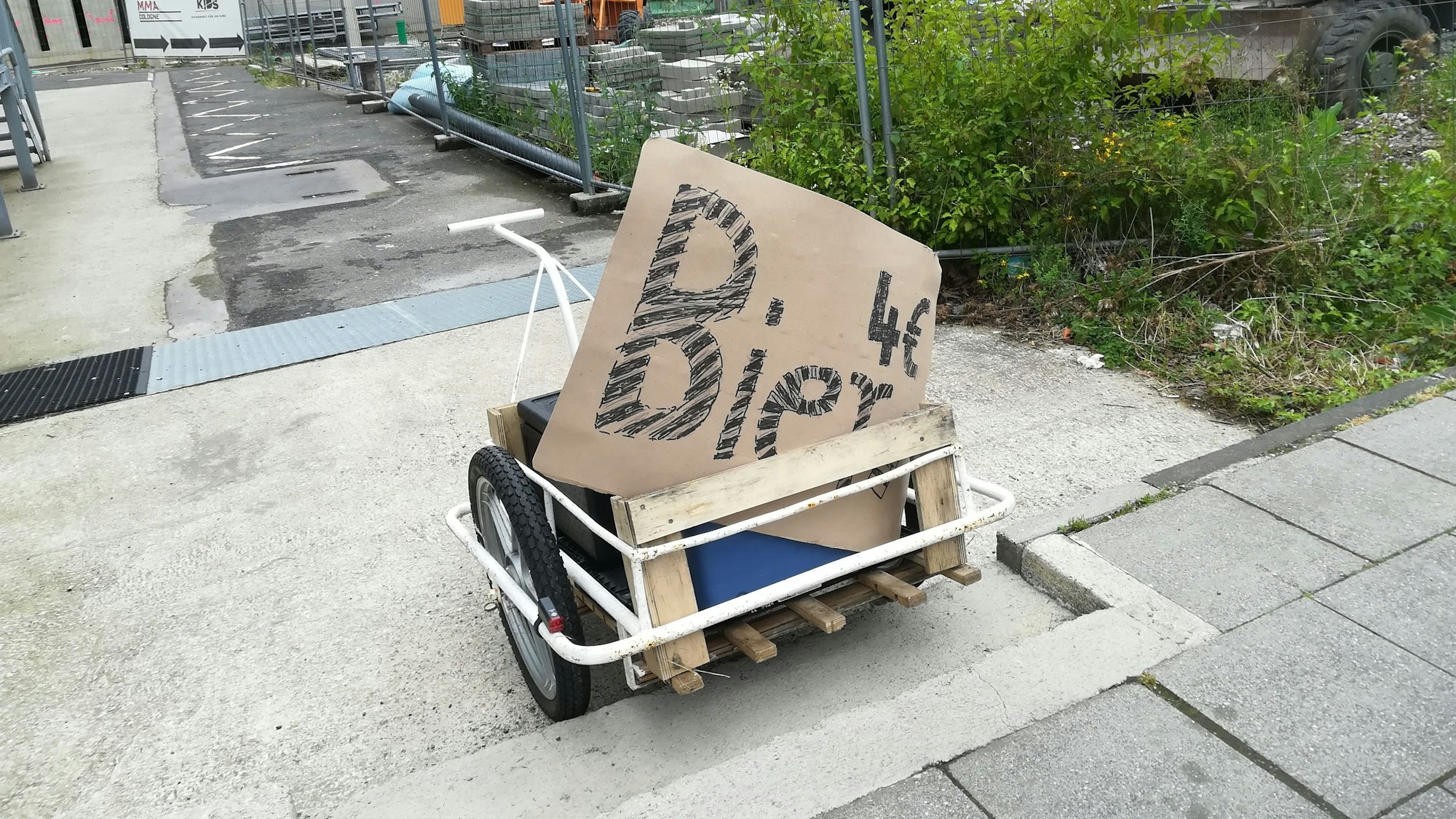 Zu sehen ist ein Anhänger, in dem ein Plakat mit der Aufschrift „Bier 4 Euro“ steht.