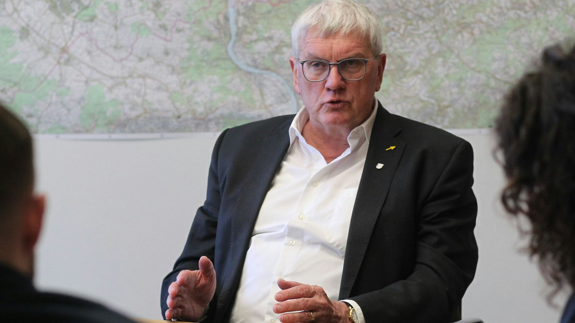 Sebastian Schuster, Landrat des Rhein-Sieg-Kreises, sitzt in seinem Büro vor einer Karte des Kreisgebietes.