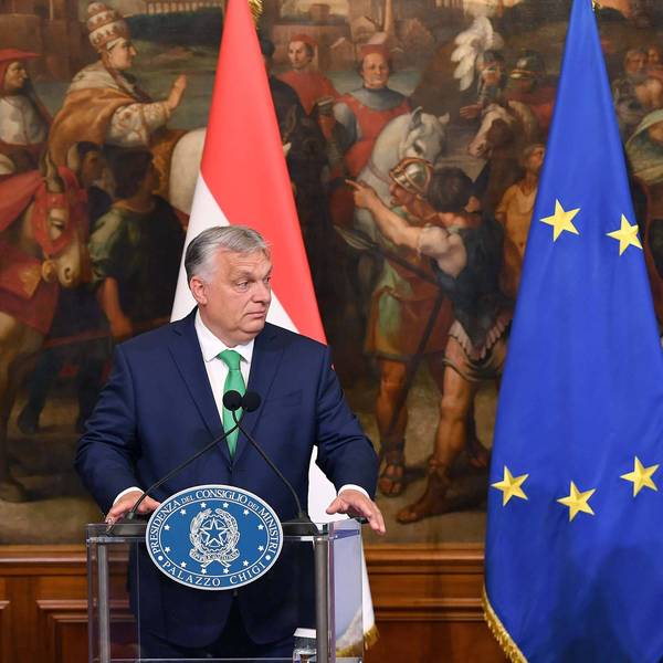 Orban und Meloni stehen an Pulten, sie haben Flaggen ihrer Länder im Hintergrund. Zwischen ihnen hängt die europäische Fahne.