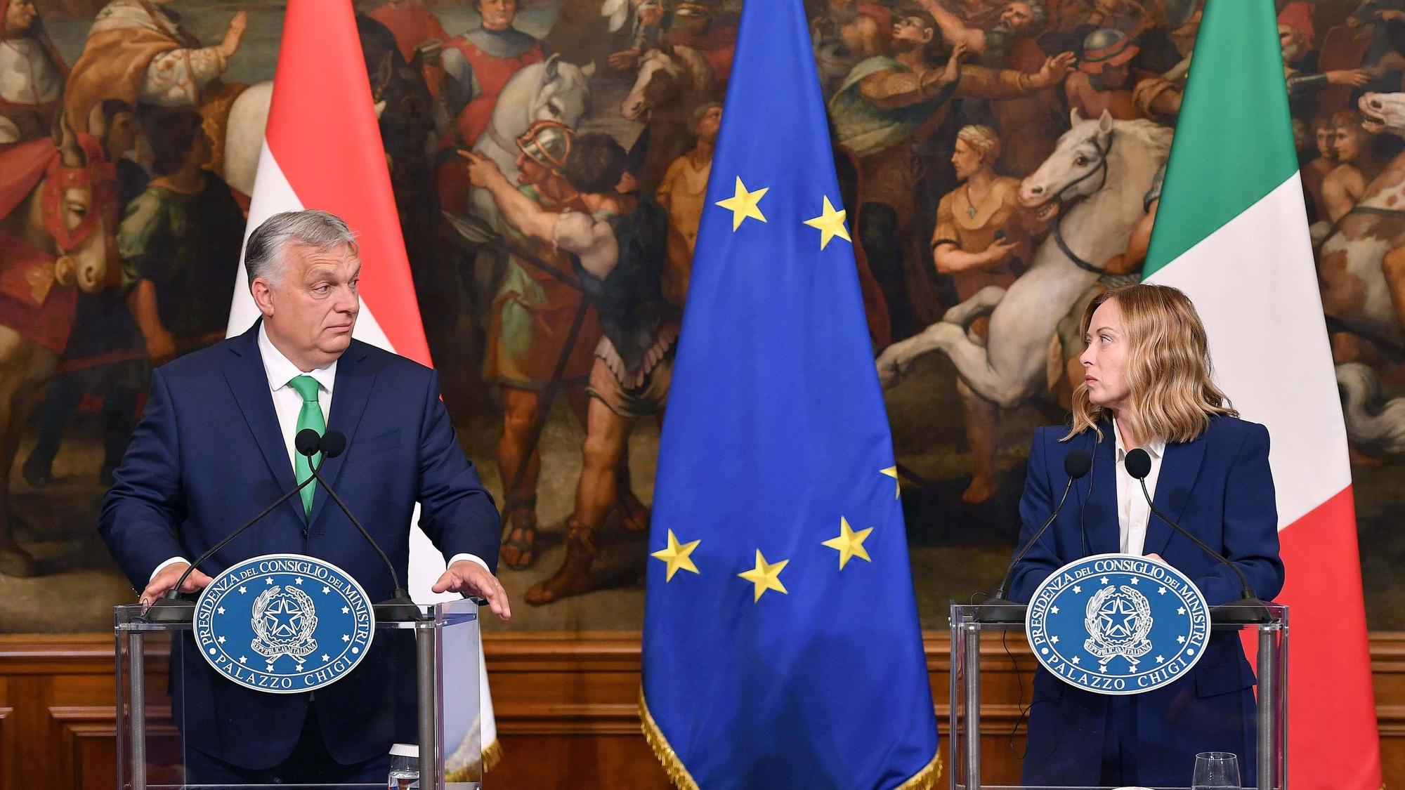 Orban und Meloni stehen an Pulten, sie haben Flaggen ihrer Länder im Hintergrund. Zwischen ihnen hängt die europäische Fahne.