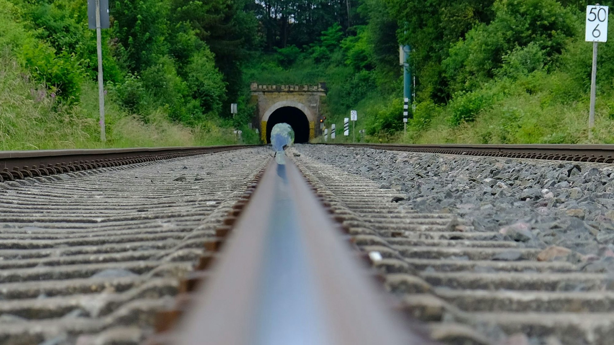 Nordseite des Kaller Eisenbahntunnels mit Schienen, Schwellen und Schotter im Vordergrund.