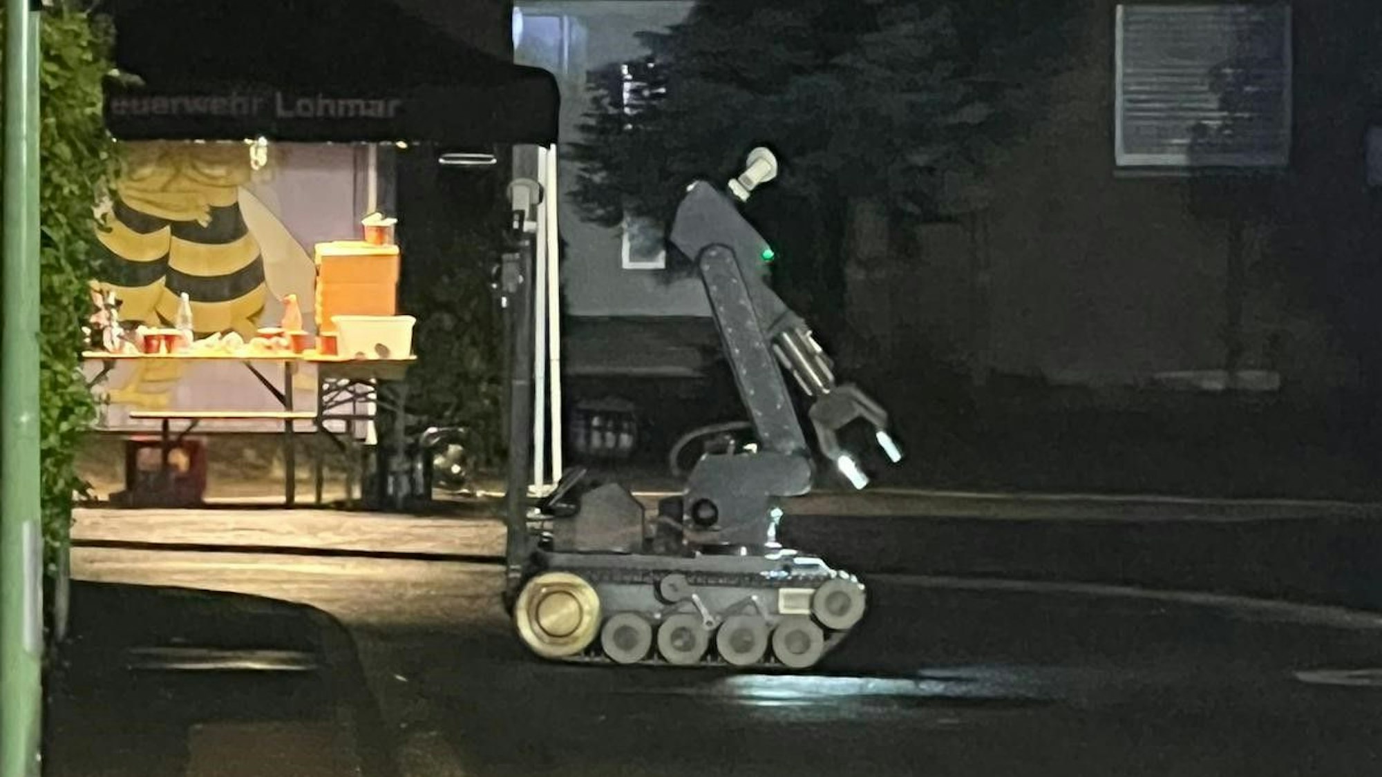 Ein Roboter auf einem Kettenantrieb und mit Greifarm rollt über eine Straße.