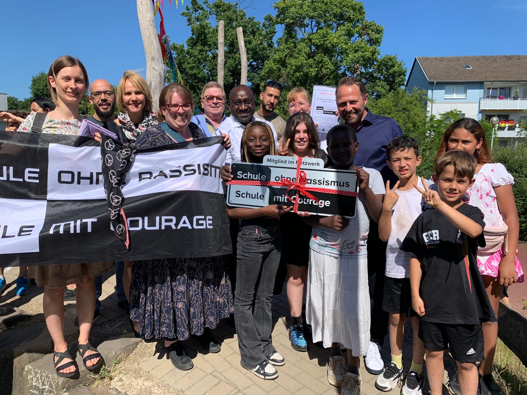 Menschen stehen zusammen und halten ein Schild mit der Aufschrift „Schule ohne Rassismus – Schule mit Courage“.