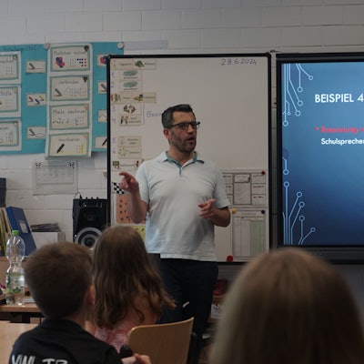 Ahmet Özdemir steht vor der Tafel in einem Klassenraum. Kinder blicken in seine Richtung.