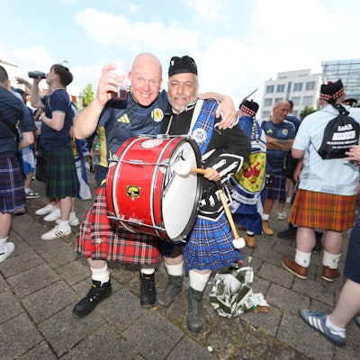 Zwei Schottland-Fans mit Pauke und im Kilt umarmen sich.
