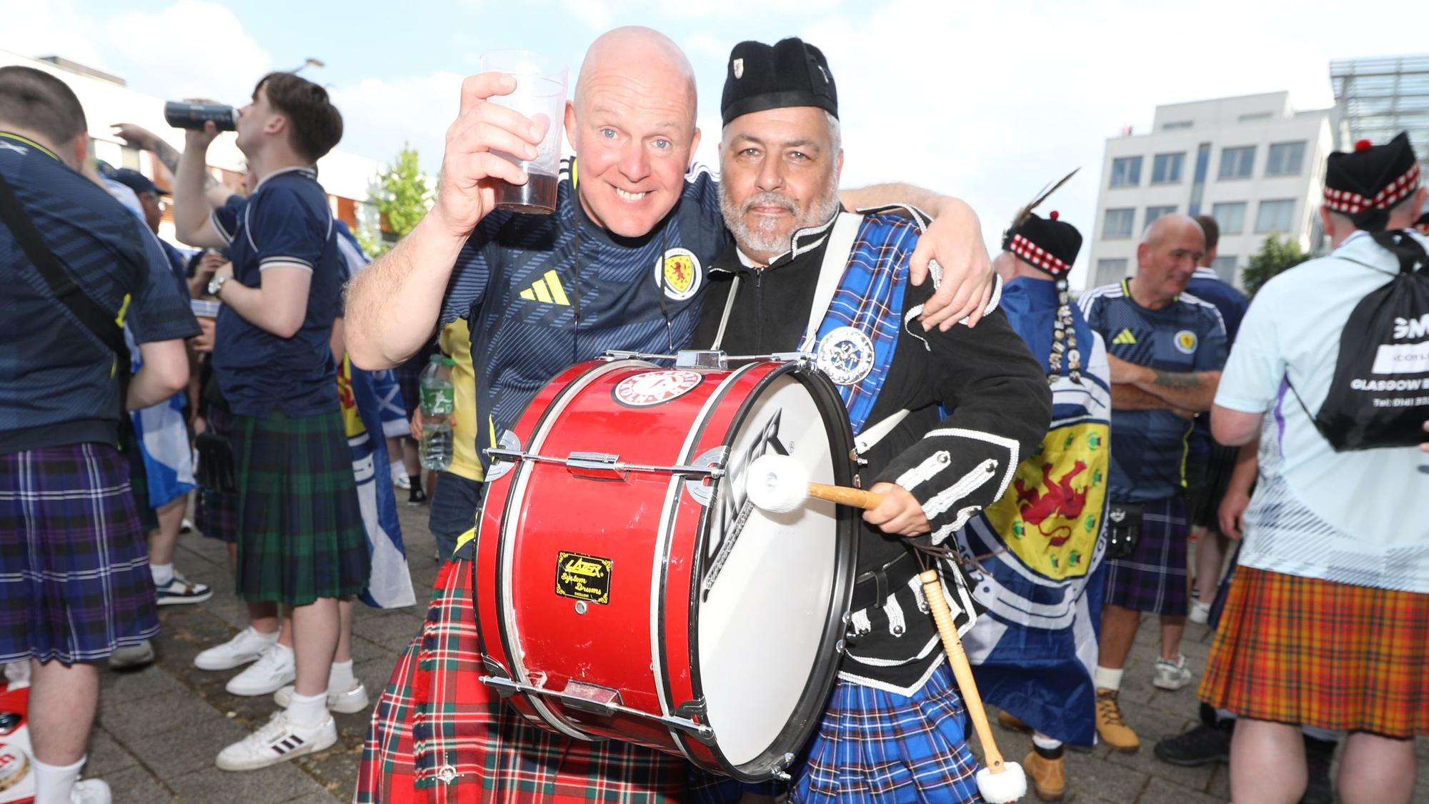 Zwei Schottland-Fans mit Pauke und im Kilt umarmen sich.