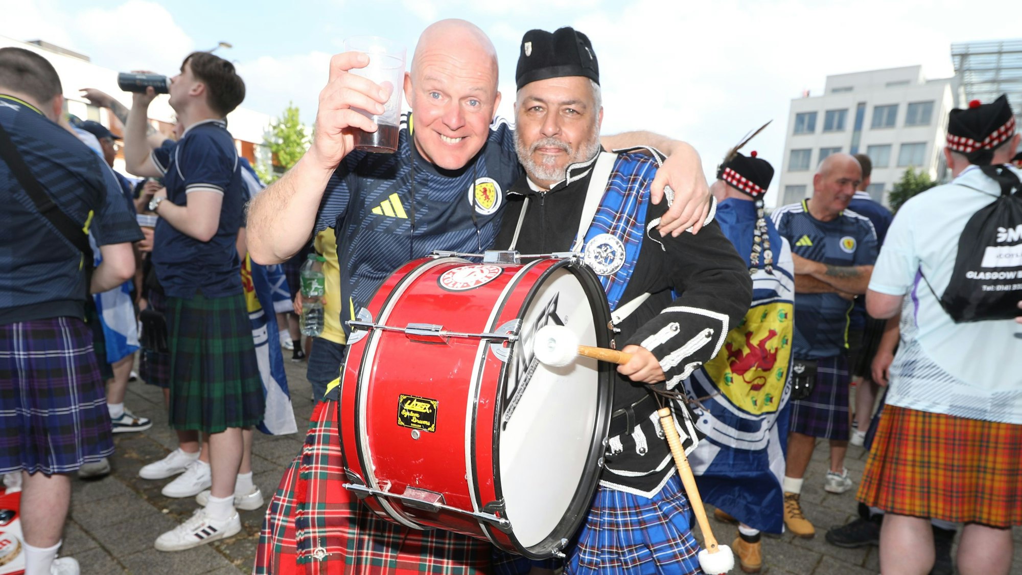 Zwei Schottland-Fans mit Pauke und im Kilt umarmen sich.