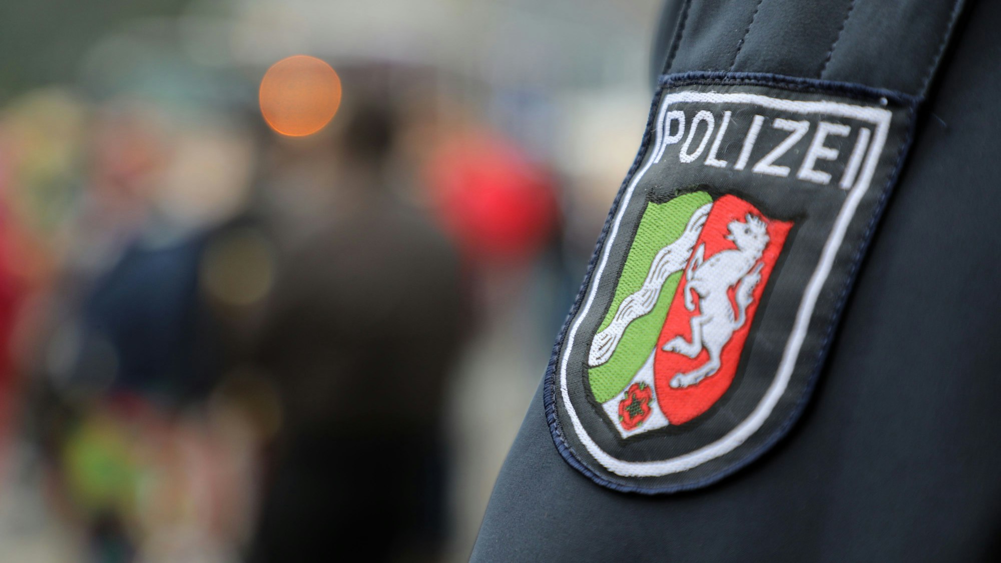 Ein Polizist steht am Straßenrand und schaut auf die Straße. Groß im Vordergrund ist sein Hoheitsabzeichen auf dem Ärmel zu sehen.