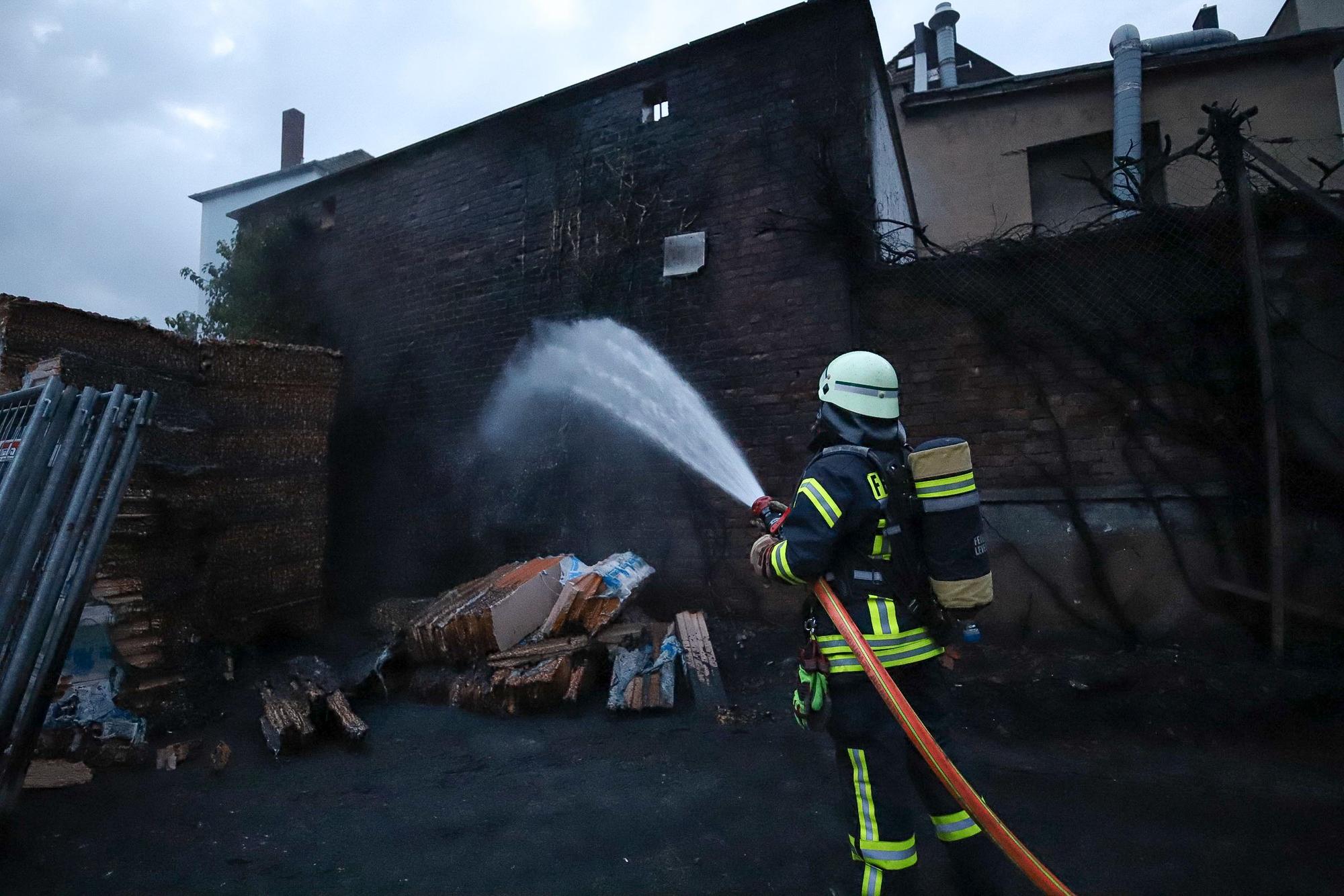 Ein Feuerwehrmann löscht vor einer verrußten Hauswand.