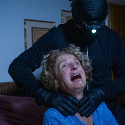 Eine Szene aus dem Film: Das Opfer wird von einem maskierten Mann am Hals gepackt, im Hintergrund steht ein ebenfalls maskierter Mann mit einem Tresor.