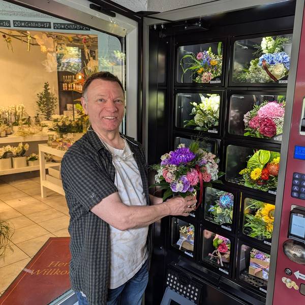 Florist Manfred Lieven mit einem Strauß in der Hand vor dem geöffneten Blumenautomaten vor dem Laden.