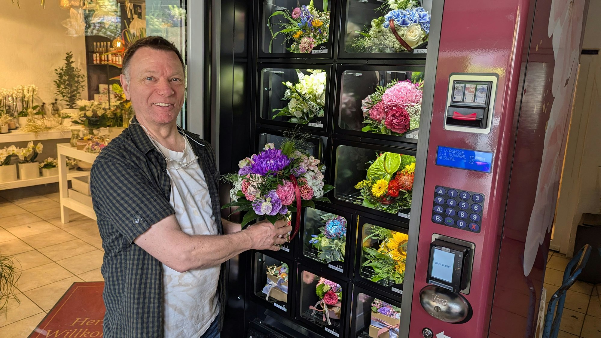 Florist Manfred Lieven mit einem Strauß in der Hand vor dem geöffneten Blumenautomaten vor dem Laden.