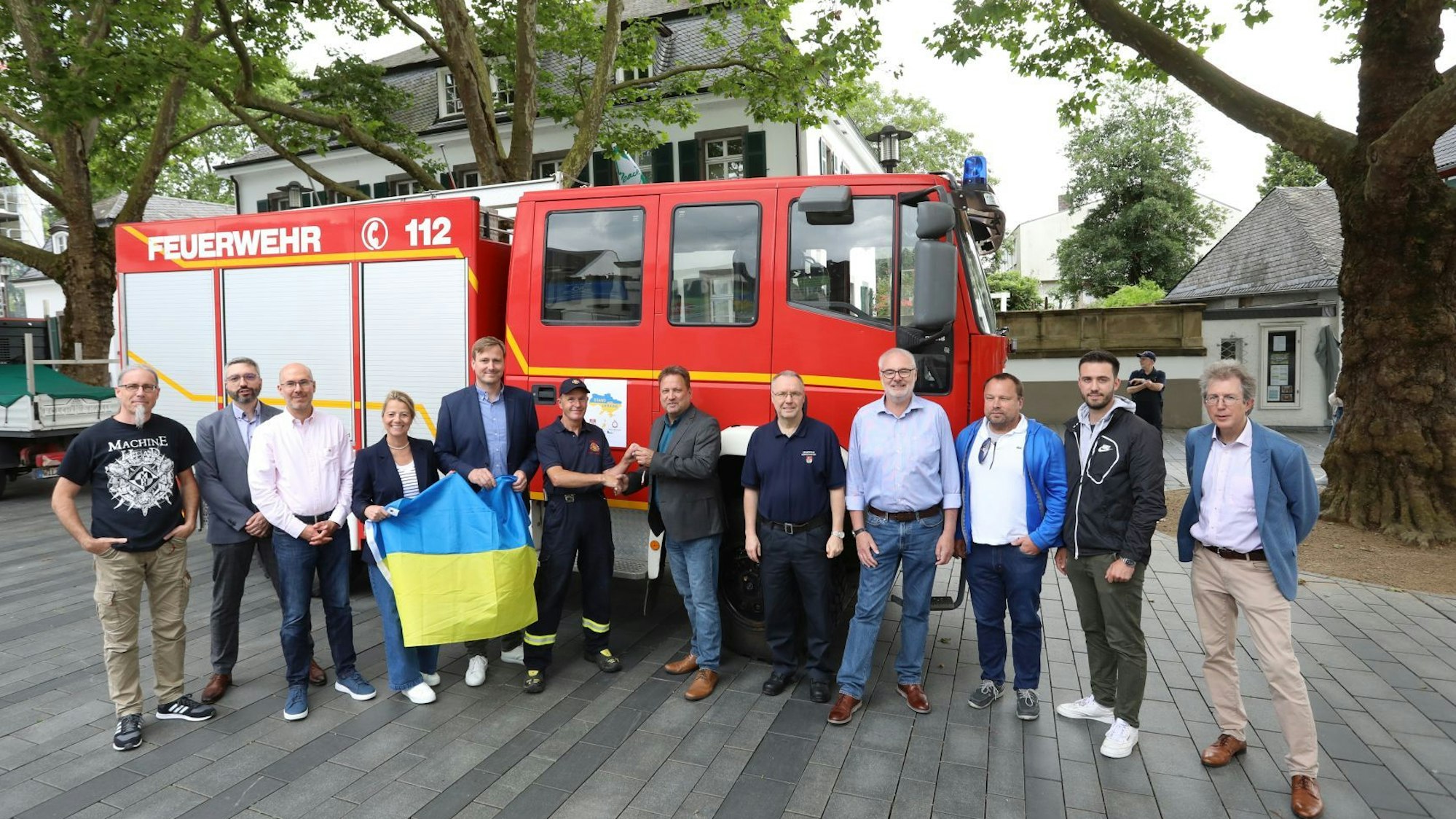 Eine Gruppe von Personen steht mit einer ukrainischen Flagge vor einem Feuerwehrfahrzeug.