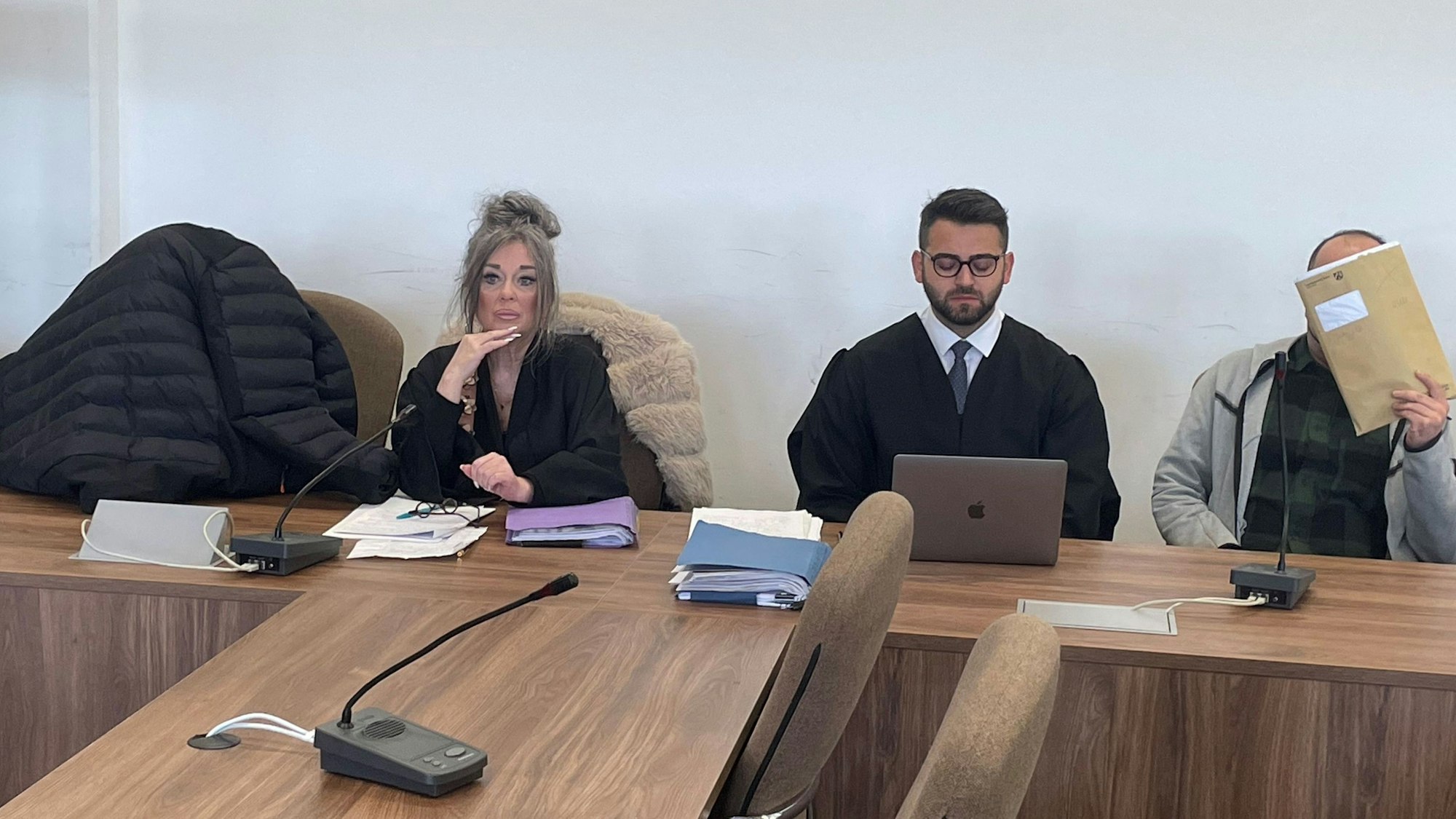 Die Angeklagten, dazwischen ihre Verteidiger, verstecken sich beim Prozessauftakt hinter einer Jacke und einer Mappe vor den Pressefotografen.