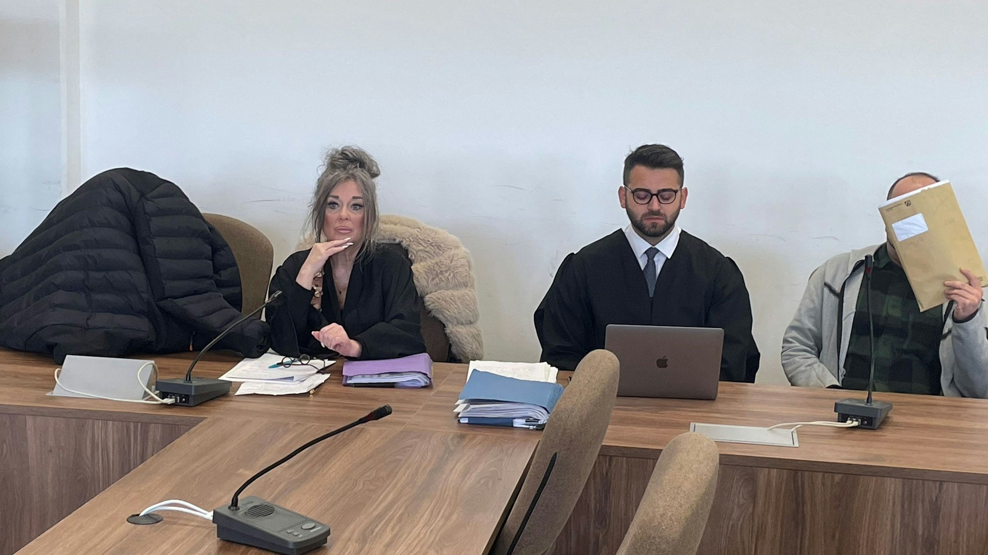 Die Angeklagten, dazwischen ihre Verteidiger, verstecken sich beim Prozessauftakt hinter einer Jacke und einer Mappe vor den Pressefotografen.