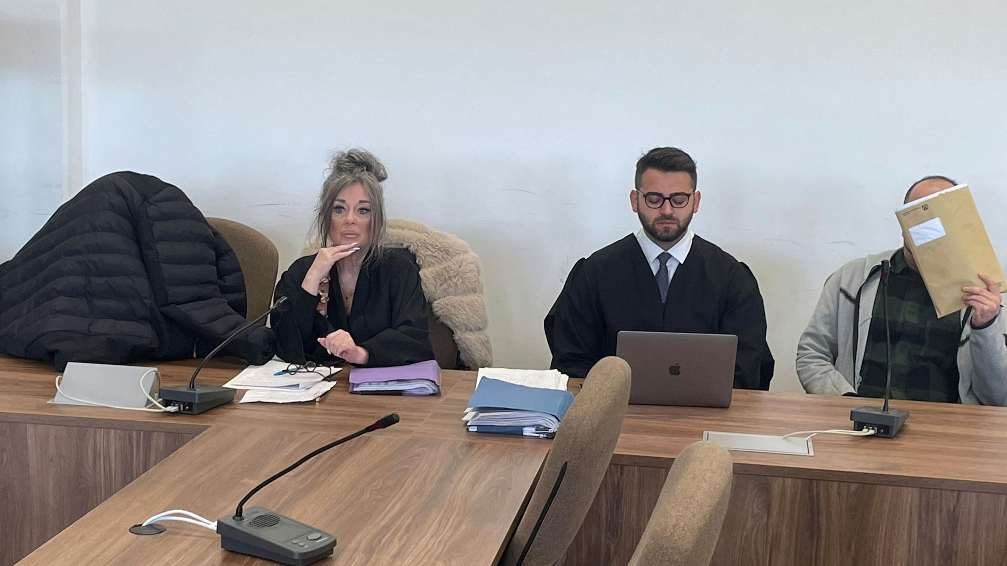 Die Angeklagten, dazwischen ihre Verteidiger, verstecken sich beim Prozessauftakt hinter einer Jacke und einer Mappe vor den Pressefotografen.