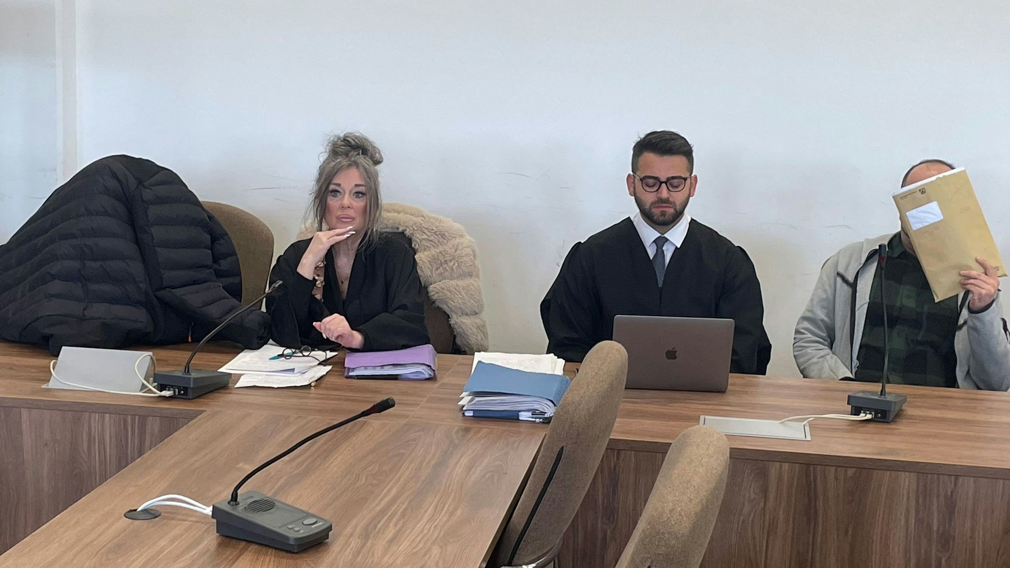 Die Angeklagten, dazwischen ihre Verteidiger, verstecken sich beim Prozessauftakt hinter einer Jacke und einer Mappe vor den Pressefotografen.