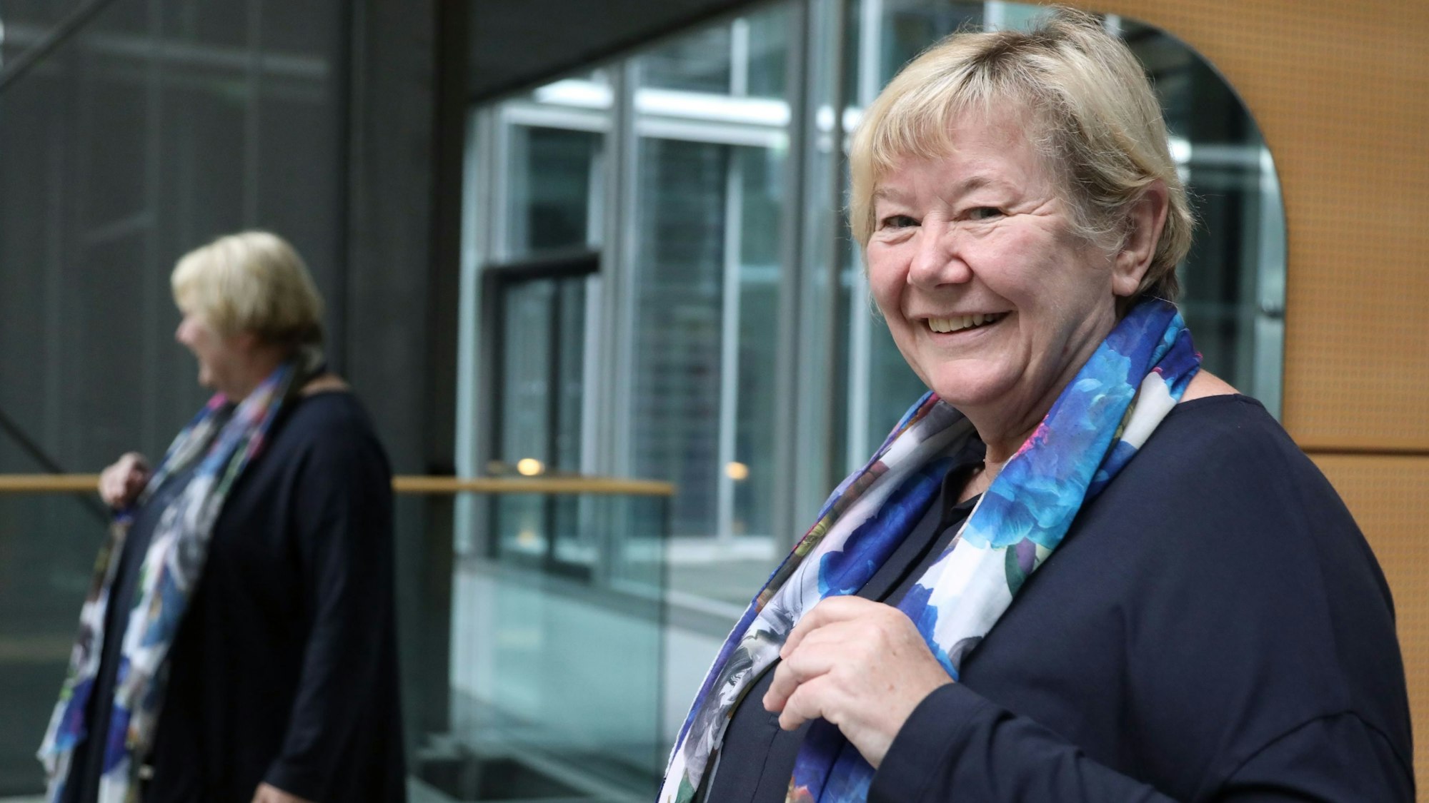 „Lobby für Mädchen“-Mitbegründerin und Geschäftsführerin Frauke Mahr steht lächelnd vor einem großen Spiegel, sie trägt ein dunkelblaues Kleid und ein blau-weißes Tuch mit Blumenprint-