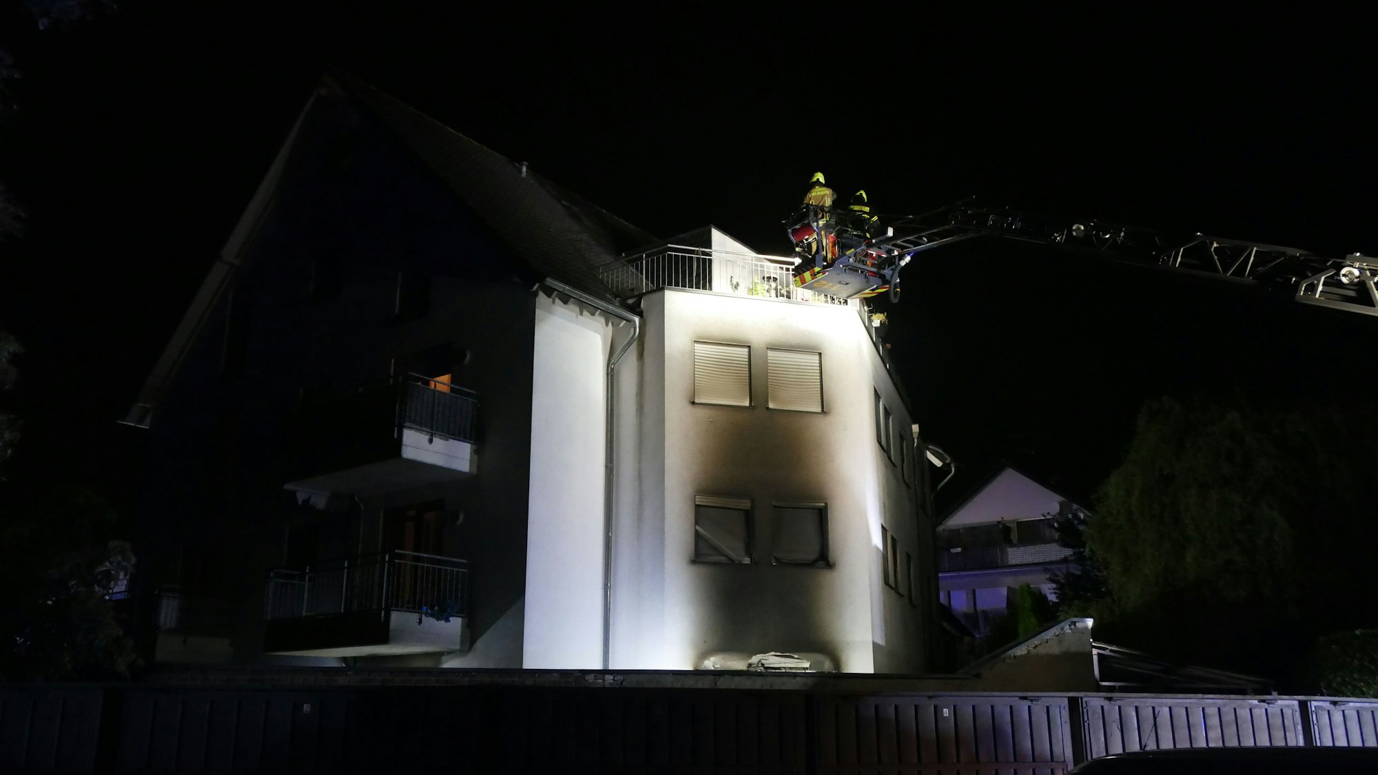 Eine geschwärzte Hausfassade, davor ein Korb einer Drehleiter der Feuerwehr.