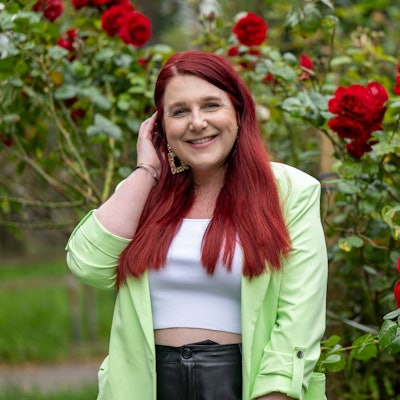 Eine Frau steht lächelnd neben einem Rosenbusch.