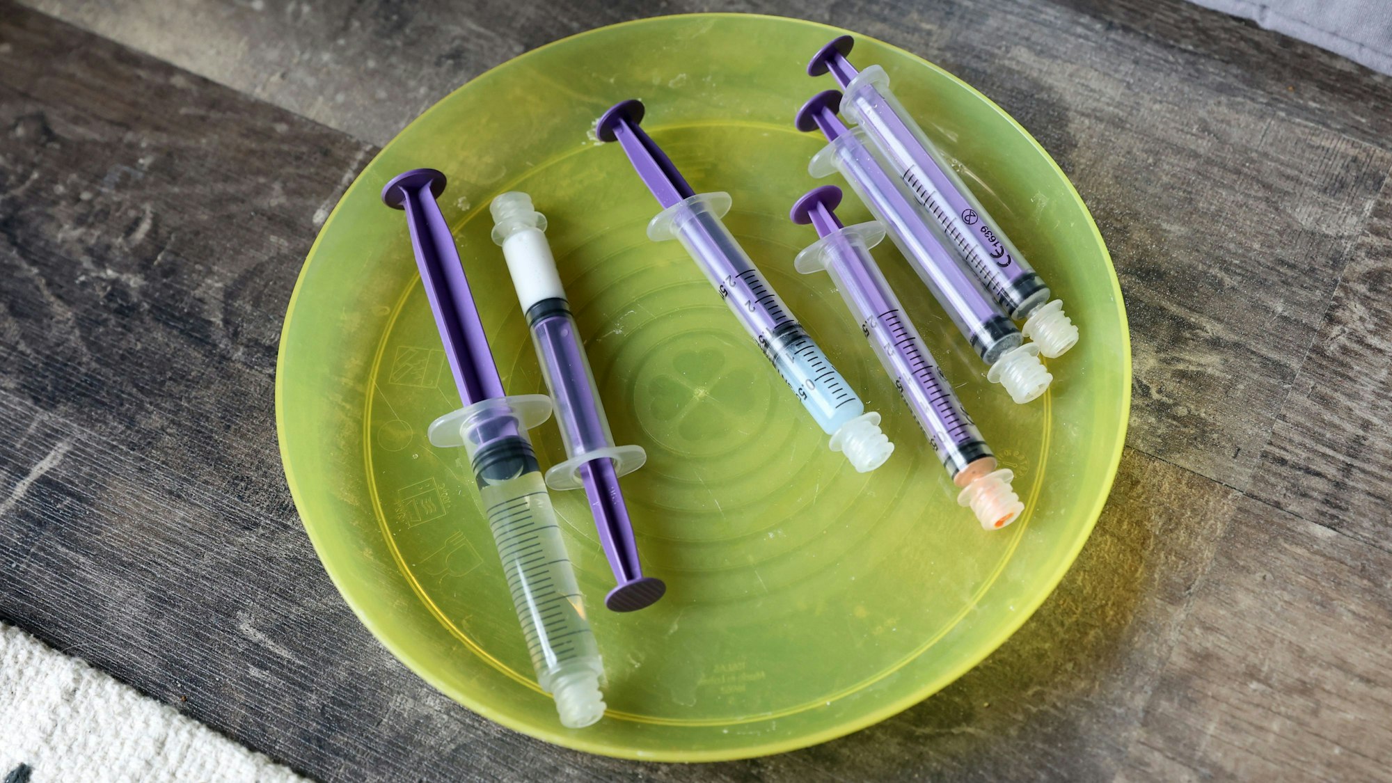 Sechs Spritzen liegen auf einem gelben Plastikteller.